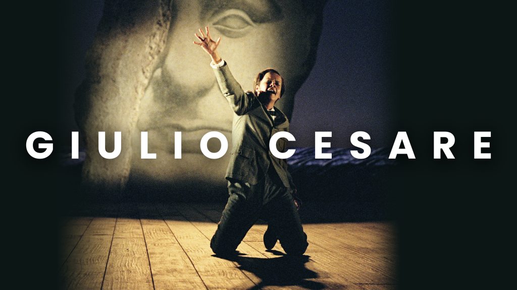 A singer dressed in a suit is kneeling on the ground with their hands outstretched above them.
